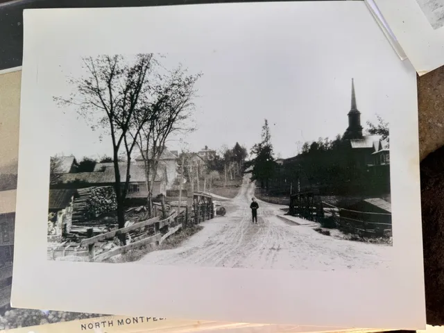 Early 1900s photo of a dirt Main Street in North Montpelier, with a church steeple and a boy standing in the road.
