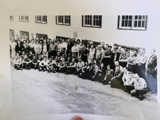 Large group photo of mill workers posed outside a mill building.